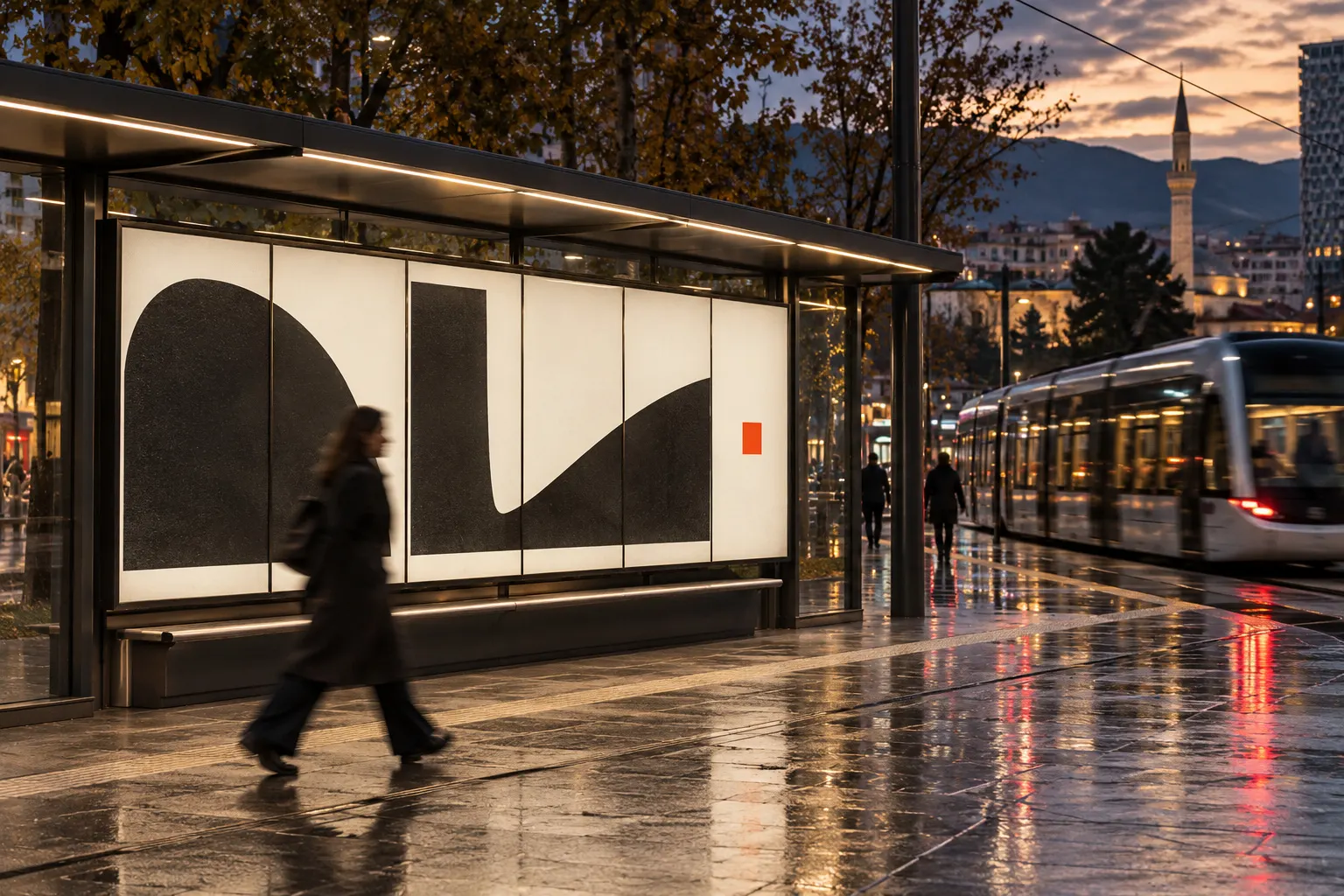 A commuter walks past a backlit tram-stop poster in Tirana on a wet evening.